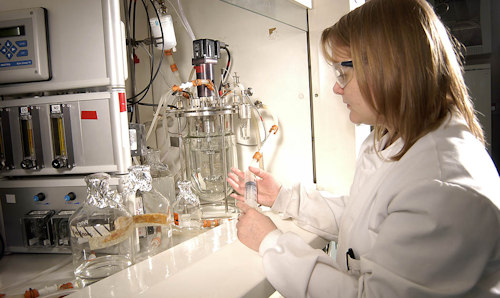 Female researcher in white coat and safety glasses using equipment